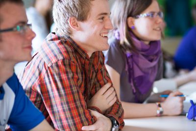 Handsome college student sitting in a classroom full of...