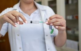 A focused nurse in a white lab coat carefully prepares a...