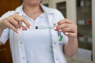 A focused nurse in a white lab coat carefully prepares a...