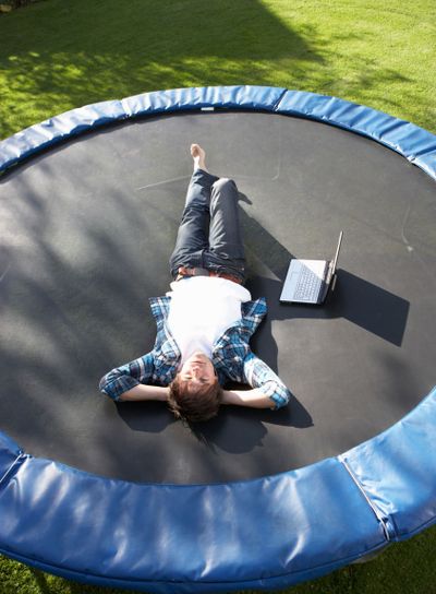Young Man Relaxing On Trampoline With Laptop