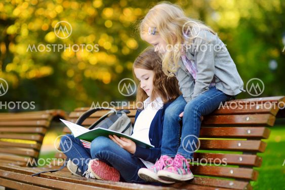 Two adorable little schoolgirls studying in a city park