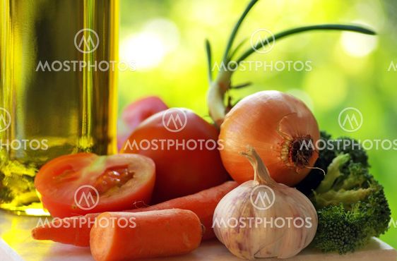 Olive oil and vegetables in green background.