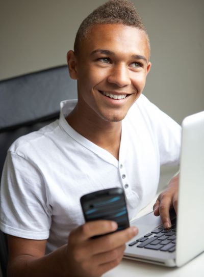 Teenage Boy Using Laptop And Mobile At Home