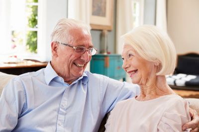 Smiling Senior Couple Sitting On Sofa At Home Together