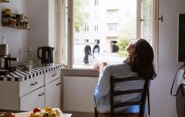 Rear view of young woman sitting on chair with feet up on window at home