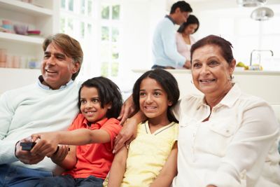 Multi-Generation Indian Family Sitting On Sofa Watching TV