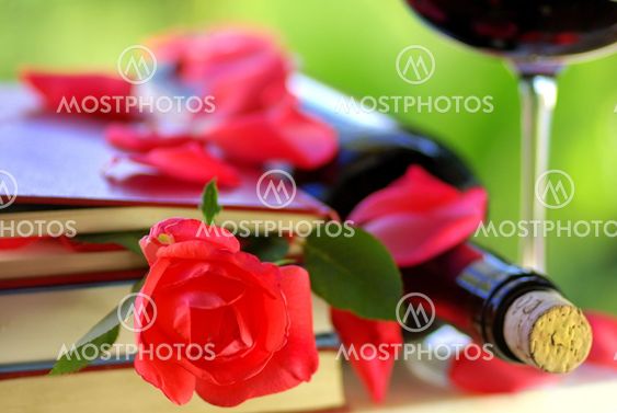 Red rose petals on books and bottle of wine.