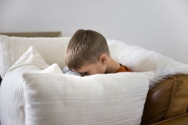 Cute little 6s boy sit on couch fenced with cushions
