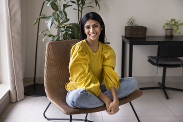 Beautiful Indian woman sitting in woven chair in relaxed...