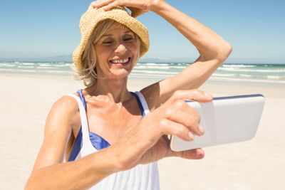 Woman using smart phone while standing at beach against...