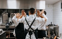 Male and female chef giving high-five to each other while standing in commercial kitchen