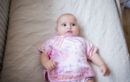Curious and adorable baby girl in Asian pink attire lying...
