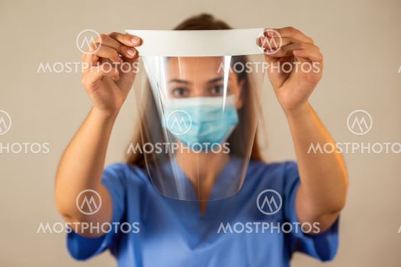Female nurse in blue shirt holding protective face...