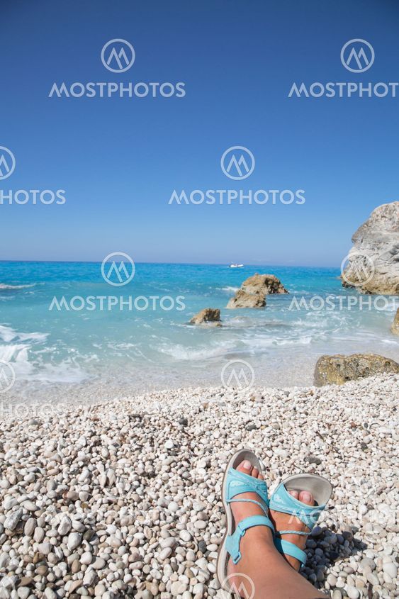 Pebble beach crossed feet and clear blue sky for a holiday background