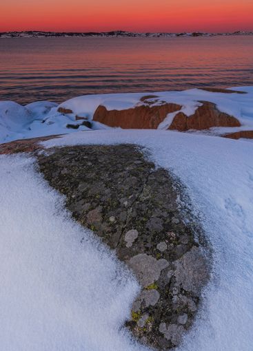 Snow-covered rocks at sunset reflect vibrant colors in a...