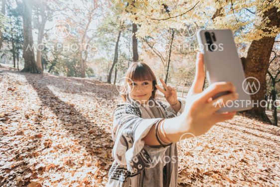 Happy girl using smart phone during Autumn in a park...