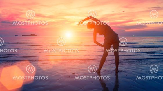 Female silhouette performs physical exercises on the beach after sunset.
