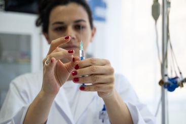 A focused nurse in a white lab coat carefully prepares a...
