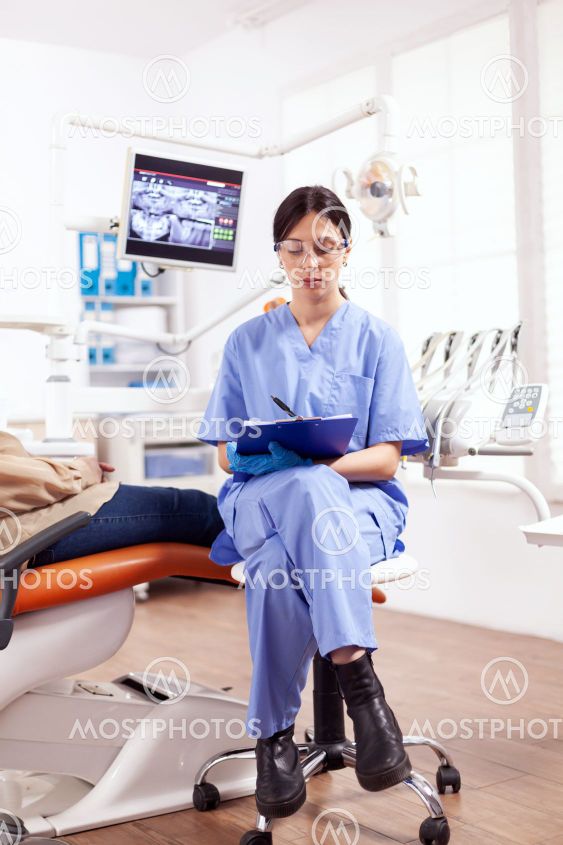 Dental assistant taking notes on clipboard in dentist...