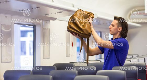 Young caucasian man putting luggage on the top shelf at...