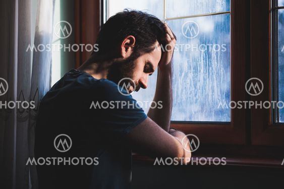 Young sad mad sitting by the window in regret