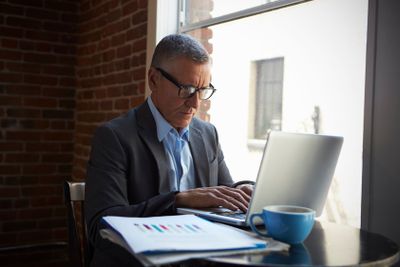 Mature Businessman Working On Laptop By Office Window