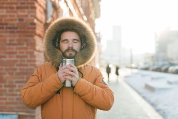 Man enjoying warm drink in sunlight on cold winter urban...