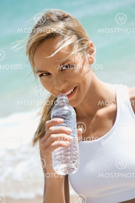 Woman drinking water on beach.