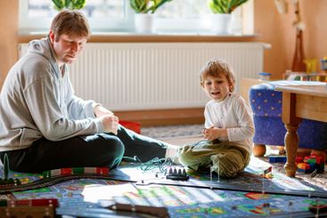 Father and son playing with racing cars on racetrack,...
