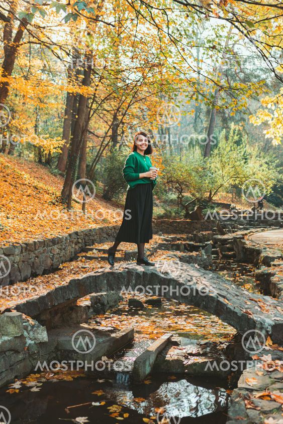 young smiling pretty woman walking by autumn city park