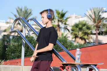 Handsome teenager standing with skateboard and listening...
