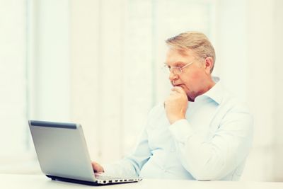 old man in eyeglasses working with laptop at home