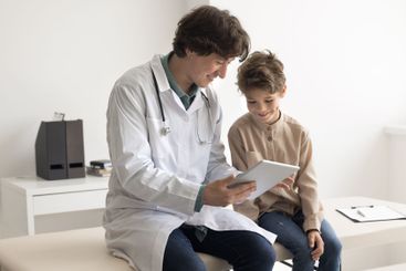 Little child sit on couch with male doctor use tablet