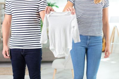 parents to be holding baby clothes