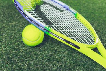 Tennis racket rests against a bright yellow ball on a...