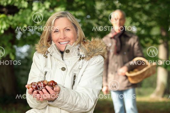 mature woman in woods with husband showing chestnuts