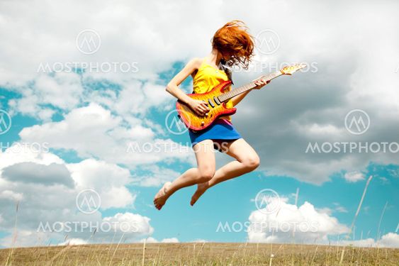 Redhead girl hoppning med gitarr vid utomhus.
