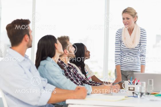 Happy team of young designers listening to boss at meeting