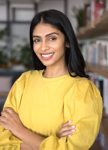 Beautiful smiling young lady posing in office with arms...