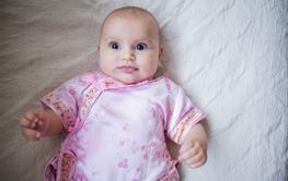 Curious and adorable baby girl in Asian pink attire lying...