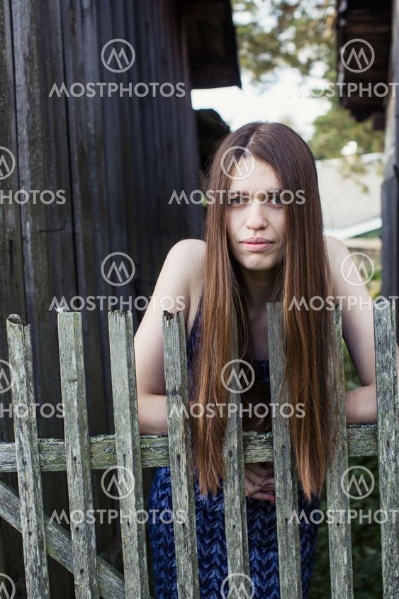 A long-haired girl stands near a wooden village fence.