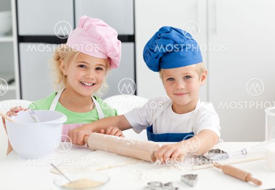 Happy brother and sister preparing a dough standing in the kitchen