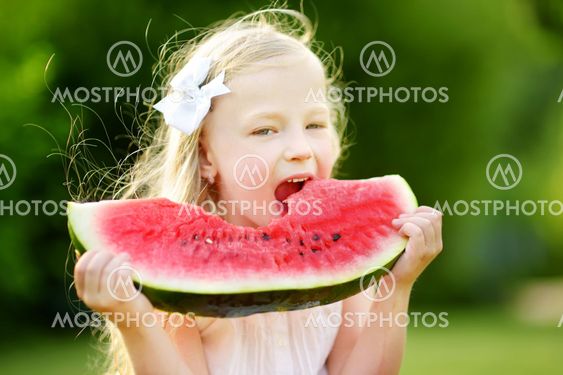 Funny little girl biting a slice of watermelon outdoors...