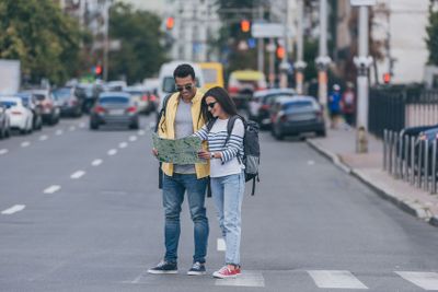Woman and multiracial friend with backpacks holding city...