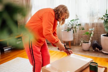 Elderly woman in orange casual clothes unpacks package....
