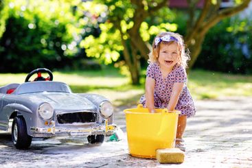 Cute gorgeous toddler girl washing big old toy car in...