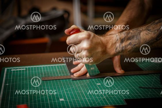 man working as artisan in his leather workshop, cutting...