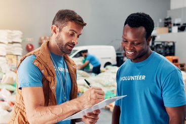 Men, volunteer and writing on clipboard at warehouse of...