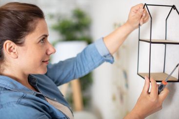 woman putting up small shelf at home using screwdriver