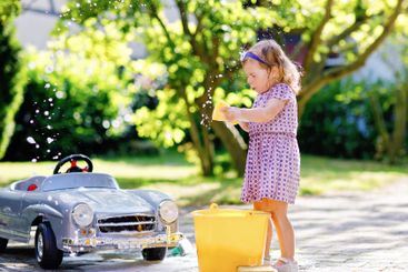 Cute gorgeous toddler girl washing big old toy car in...